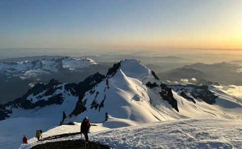 A rope team descends a glaciated mountain at sunset.