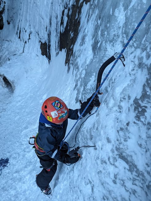 A young boy ice climbs close to the ground. The camera is above him, shooting down to show concentration on his face.