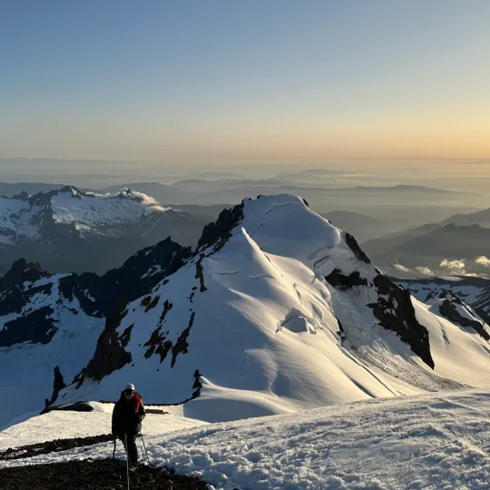 A rope team descends a glaciated mountain at sunset.