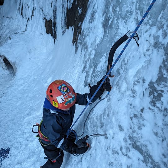 A young boy ice climbs close to the ground. The camera is above him, shooting down to show concentration on his face.